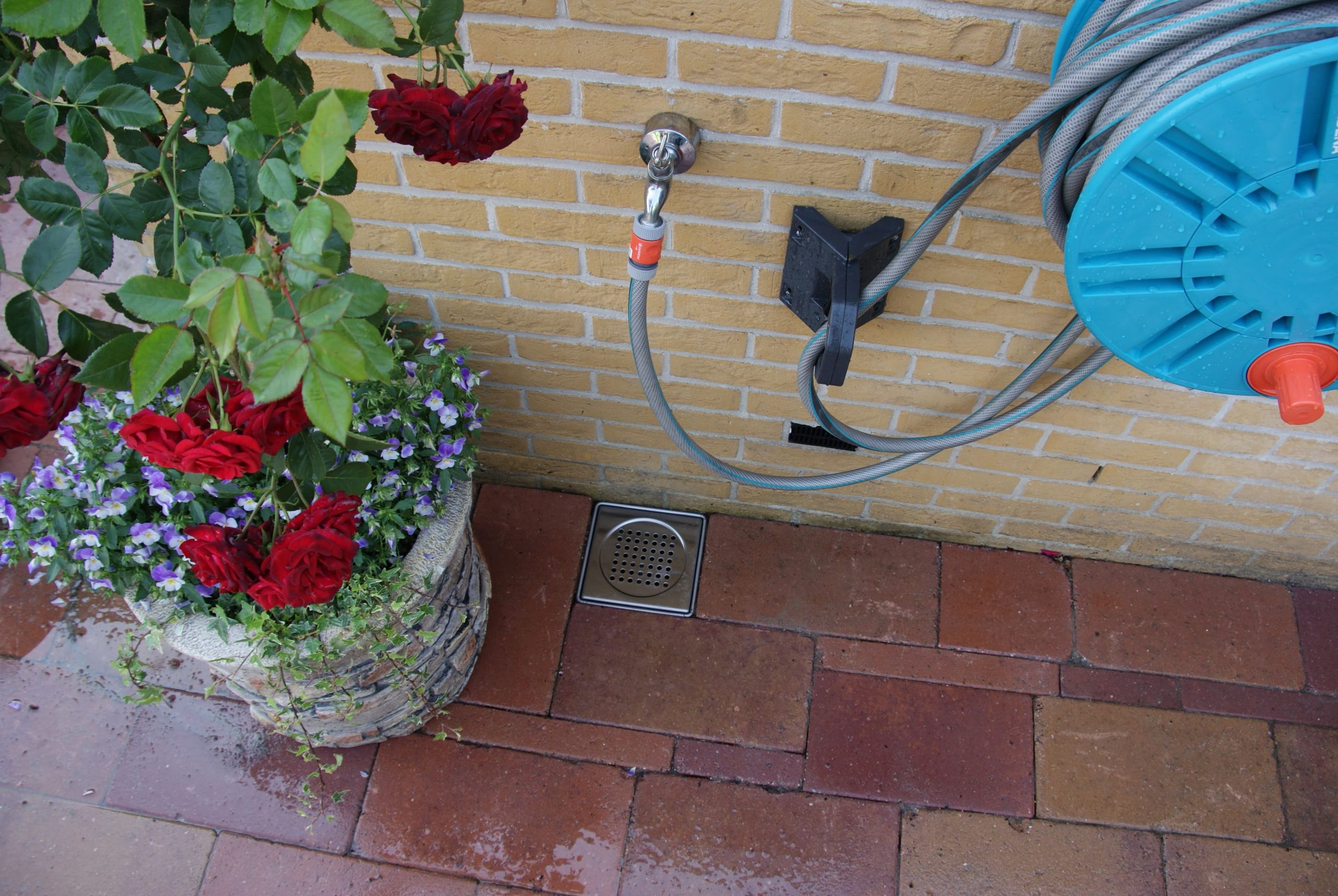 Tuinslang met afvoerputje naast bloempot.